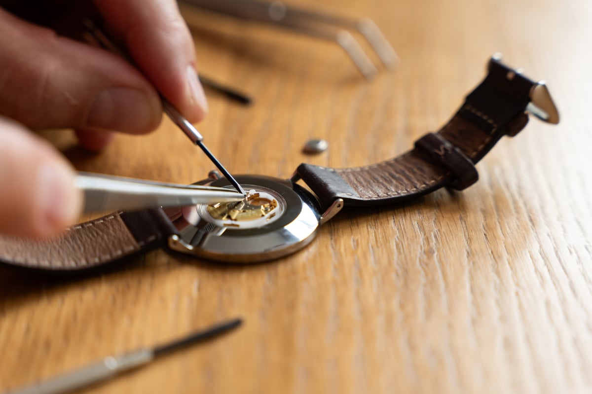 Watchmaker carefully repairing a watch movement with tweezers on a wooden workbench